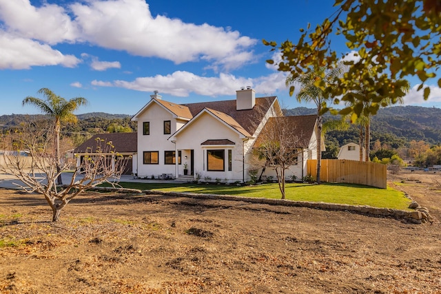 view of front of house featuring a chimney, stucco siding, fence, a mountain view, and a front lawn