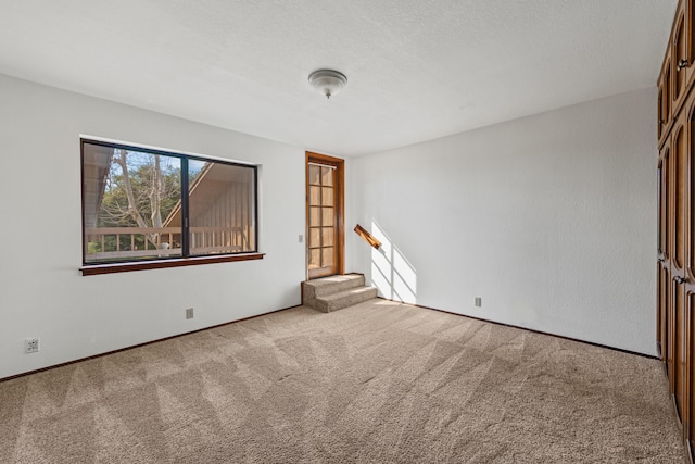 empty room with stairway, light colored carpet, and a textured ceiling