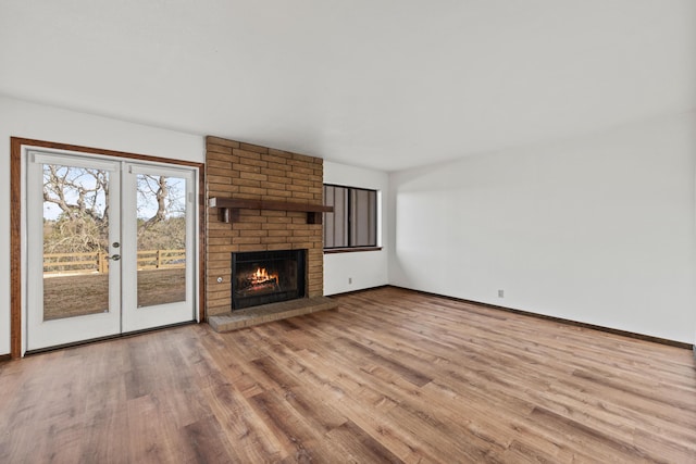 unfurnished living room featuring baseboards, french doors, light wood-type flooring, and a brick fireplace