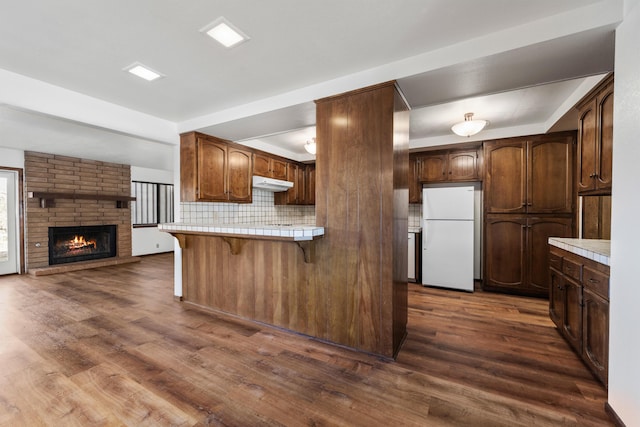 kitchen with dark wood finished floors, a breakfast bar area, open floor plan, freestanding refrigerator, and under cabinet range hood