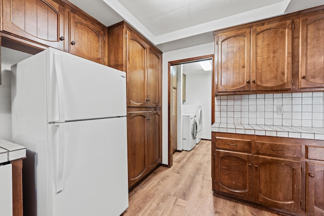 kitchen with light wood-style flooring, brown cabinets, tile counters, freestanding refrigerator, and washing machine and clothes dryer