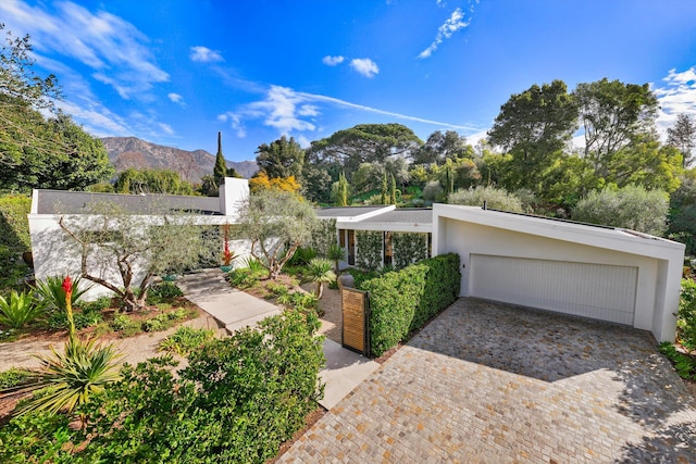 mid-century inspired home with decorative driveway, a mountain view, an attached garage, and stucco siding