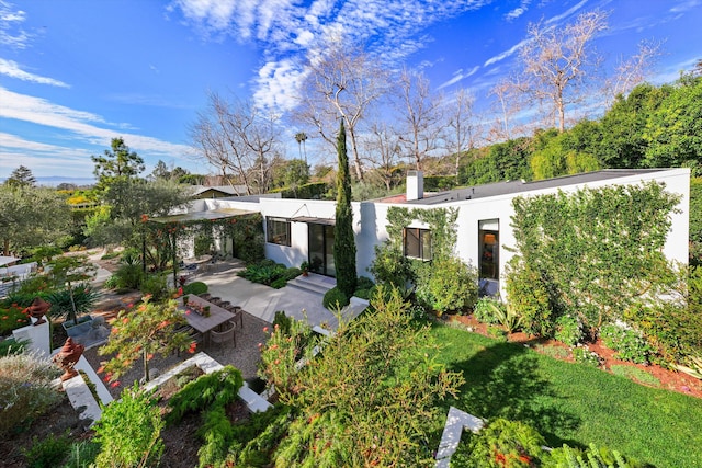 view of front of property with a chimney, a front lawn, a patio, and stucco siding