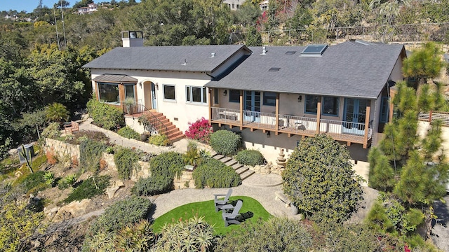 rear view of house with a shingled roof, stucco siding, a chimney, and stairs