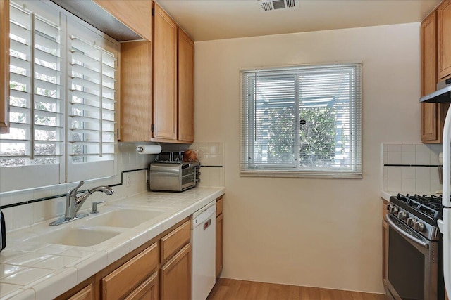 kitchen featuring white dishwasher, a sink, tile counters, decorative backsplash, and gas range