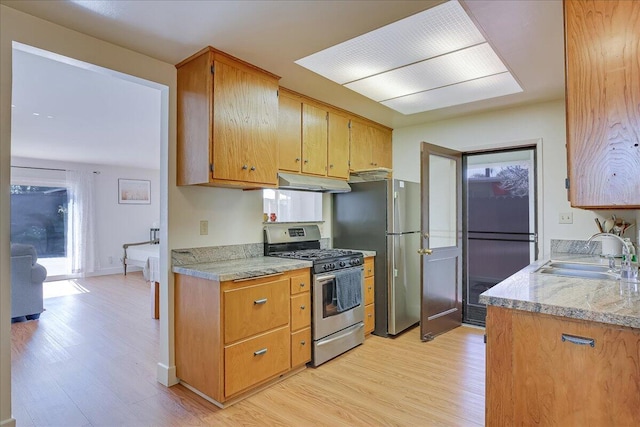 kitchen with light wood finished floors, brown cabinetry, stainless steel appliances, under cabinet range hood, and a sink