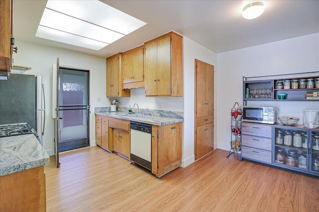 kitchen featuring stove, freestanding refrigerator, white dishwasher, light wood-type flooring, and a sink