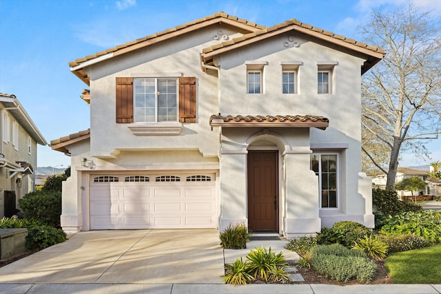 mediterranean / spanish home featuring an attached garage, driveway, a tiled roof, and stucco siding