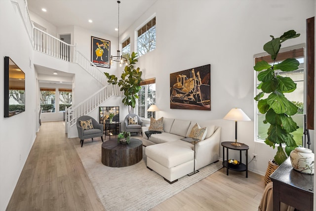 living area with recessed lighting, a towering ceiling, light wood-type flooring, baseboards, and stairs