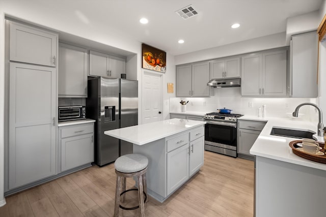 kitchen with gray cabinetry, appliances with stainless steel finishes, a sink, and under cabinet range hood