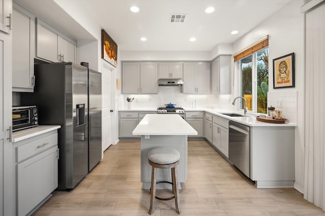 kitchen featuring visible vents, gray cabinetry, appliances with stainless steel finishes, a sink, and under cabinet range hood