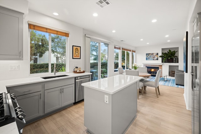 kitchen with light wood-style flooring, visible vents, appliances with stainless steel finishes, gray cabinets, and a glass covered fireplace