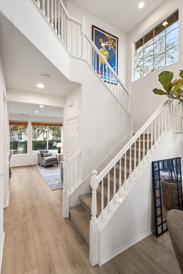 staircase with recessed lighting, baseboards, a high ceiling, and wood finished floors