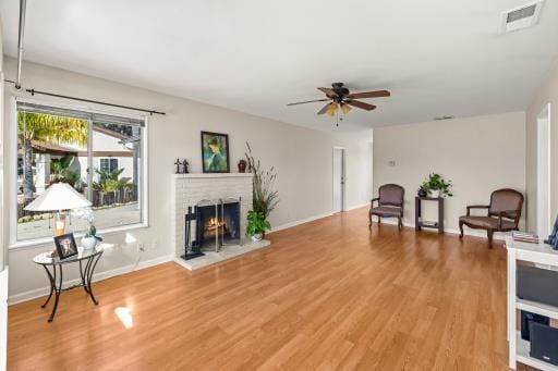 sitting room with a ceiling fan, a brick fireplace, visible vents, and light wood finished floors