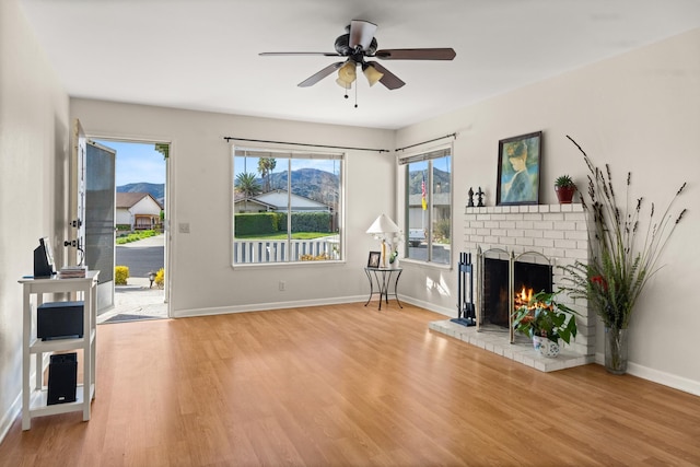 living area with ceiling fan, a fireplace, wood finished floors, and baseboards