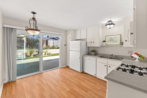 kitchen with pendant lighting, light wood finished floors, freestanding refrigerator, white cabinets, and a sink