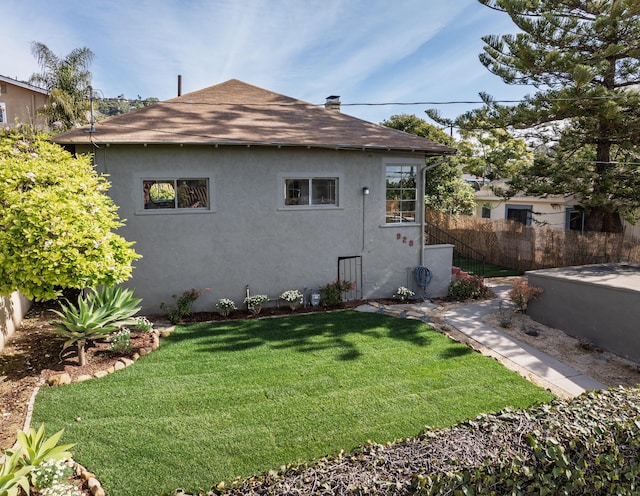 view of side of property featuring stucco siding, fence, a chimney, and a lawn