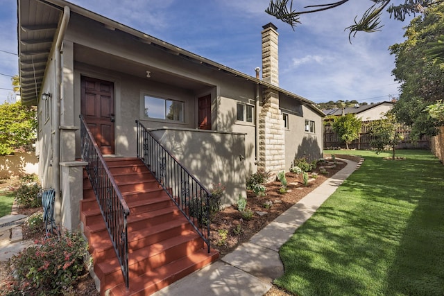 view of front facade featuring a front lawn, a chimney, fence, and stucco siding