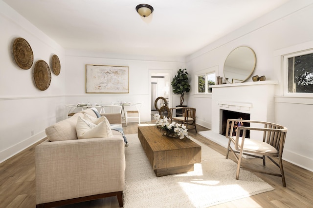 living area with a lit fireplace, baseboards, and wood finished floors