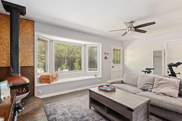 living room with visible vents, baseboards, dark wood finished floors, a ceiling fan, and a wood stove