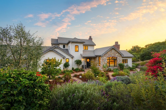 view of front of house with stone siding, a chimney, a tiled roof, and stucco siding