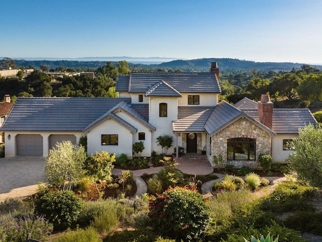 view of front of house featuring a chimney, driveway, stone siding, a mountain view, and a garage
