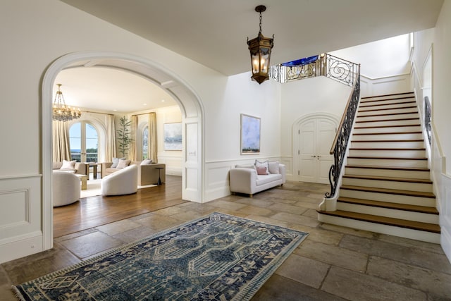 771 Garden Ln, Montecito, CA 93108 - foyer featuring arched walkways, stone tile floors, a decorative wall, an inviting chandelier, and stairs