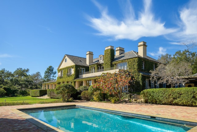 rear view of house featuring a balcony, a chimney, and an outdoor pool