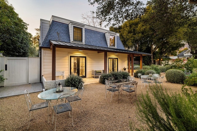 back of house at dusk with french doors, a standing seam roof, a patio area, metal roof, and fence