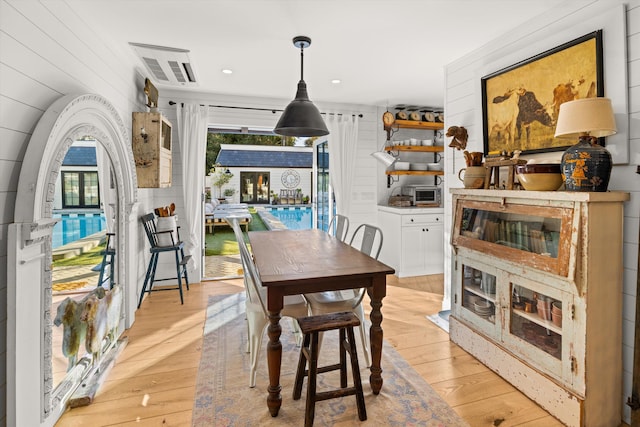 dining area featuring visible vents, wood walls, and light wood-style flooring