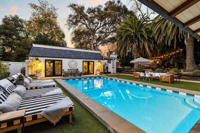 pool at dusk with an outdoor pool, an exterior structure, an outdoor structure, and fence