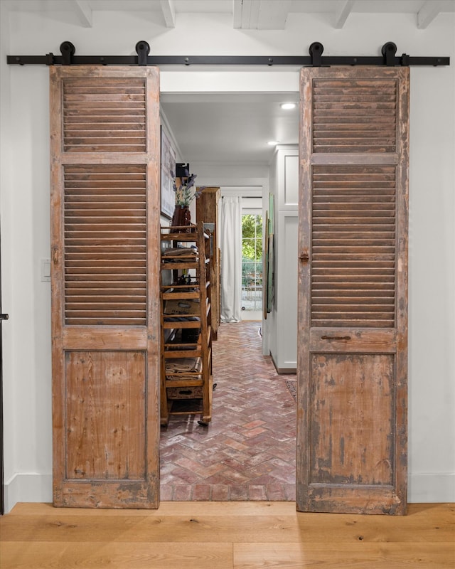 corridor featuring brick floor, a barn door, baseboards, and beam ceiling