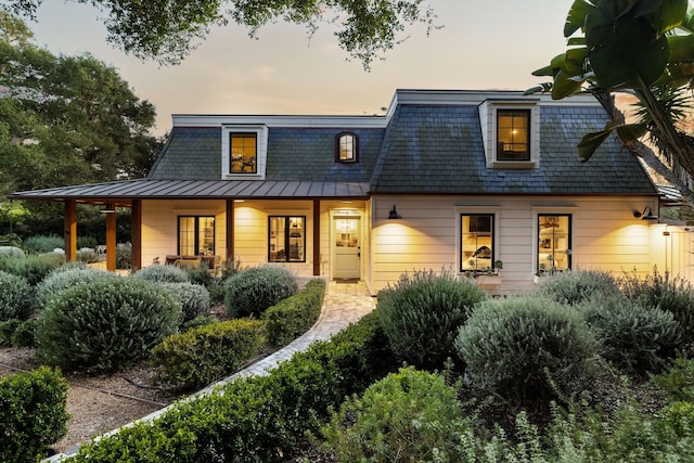 back of house at dusk featuring metal roof, mansard roof, a standing seam roof, and a porch