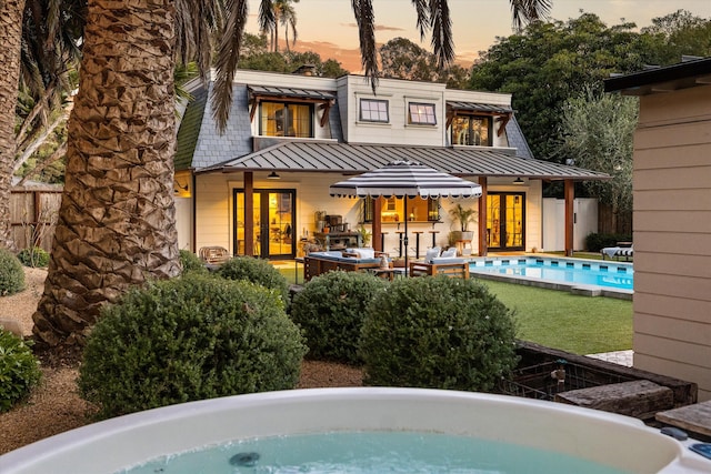 back of property at dusk with french doors, a standing seam roof, metal roof, fence, and an outdoor pool