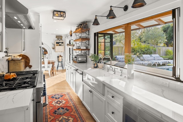 kitchen with white cabinets, light stone countertops, extractor fan, stovetop, and a sink