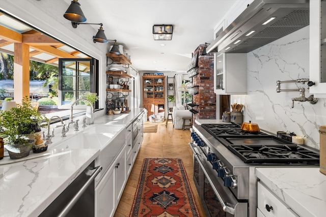 kitchen featuring wall chimney exhaust hood, appliances with stainless steel finishes, white cabinetry, and light stone counters