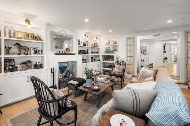 living area with built in features, ornamental molding, light wood-style floors, a fireplace, and recessed lighting