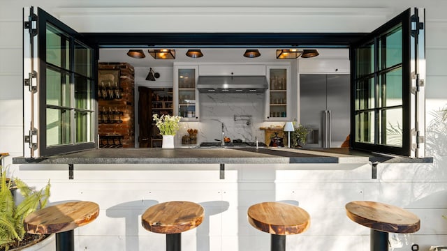 bar with stainless steel appliances, range hood, decorative backsplash, and wet bar