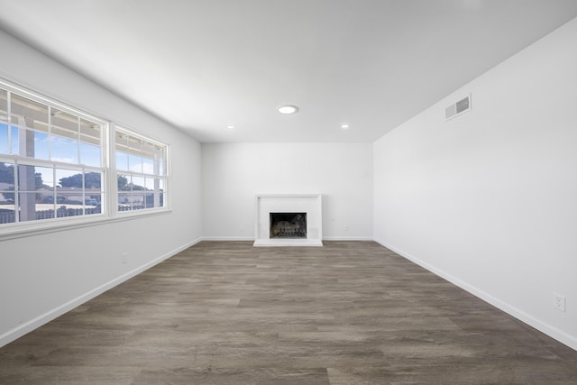 unfurnished living room featuring recessed lighting, visible vents, a fireplace with raised hearth, dark wood-type flooring, and baseboards