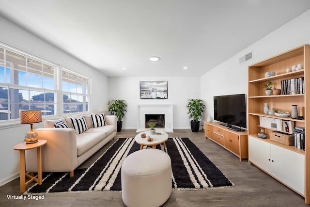 living room featuring a fireplace with raised hearth, recessed lighting, dark wood-type flooring, visible vents, and baseboards