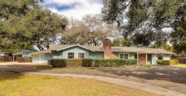 ranch-style home featuring driveway, a chimney, and fence