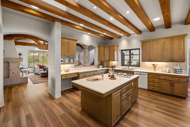 kitchen with arched walkways, dark wood finished floors, a center island with sink, light countertops, and white appliances