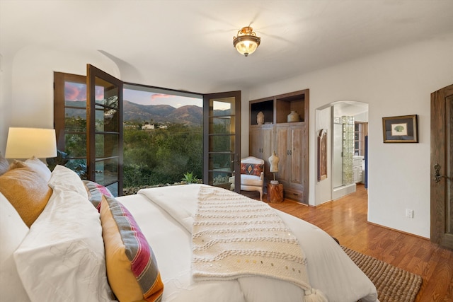 bedroom with access to exterior, arched walkways, and wood finished floors