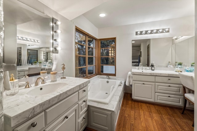 full bathroom with a whirlpool tub, two vanities, a sink, and wood finished floors