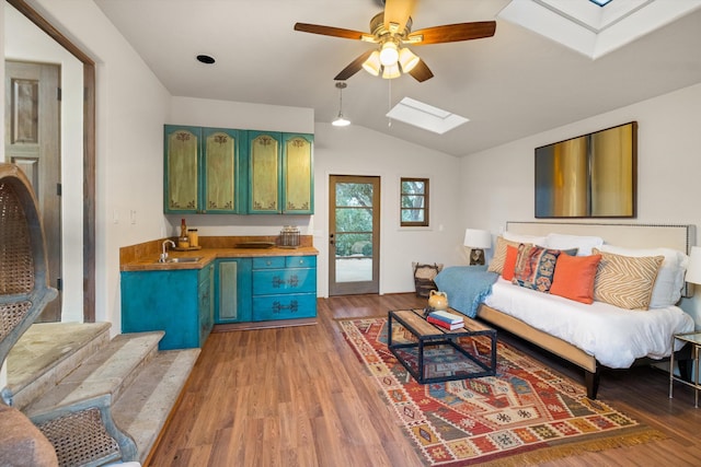 living area featuring vaulted ceiling with skylight, ceiling fan, and wood finished floors