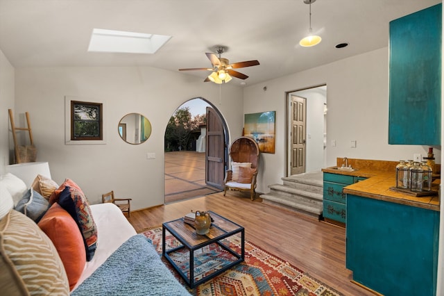 living area with stairs, vaulted ceiling with skylight, ceiling fan, and wood finished floors