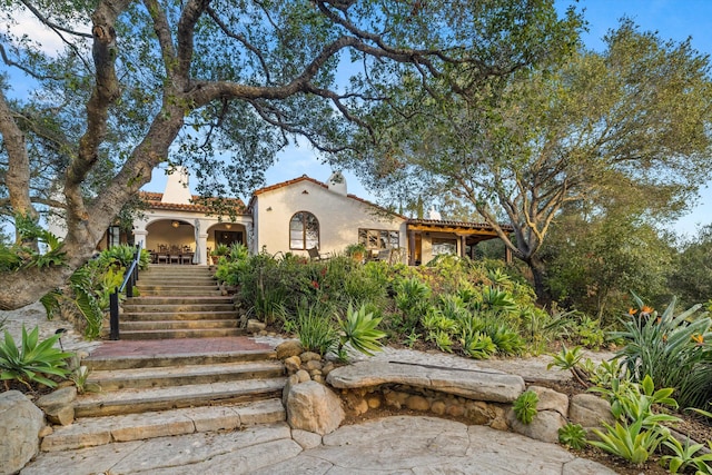 mediterranean / spanish-style home featuring stairway, a tiled roof, and stucco siding