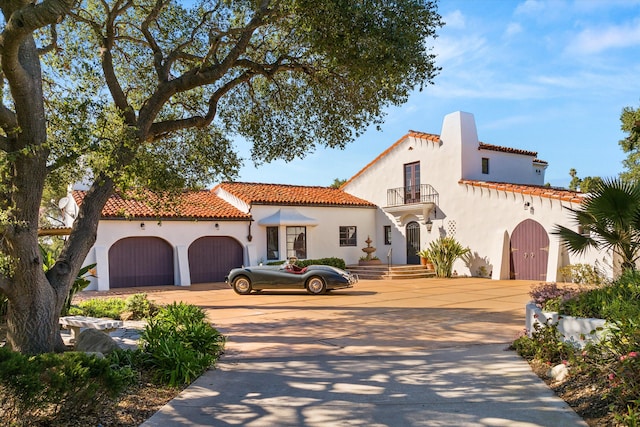 mediterranean / spanish home with driveway, an attached garage, a balcony, and stucco siding