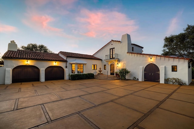 back of house with an attached garage, driveway, a tiled roof, stucco siding, and a chimney