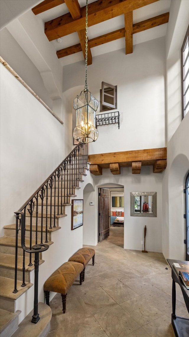 entrance foyer featuring arched walkways, beam ceiling, a towering ceiling, and stairs